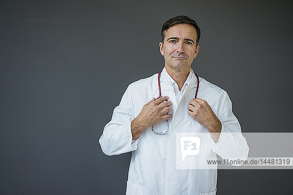 Porträt eines selbstbewussten Arztes  der an einer grauen Wand steht