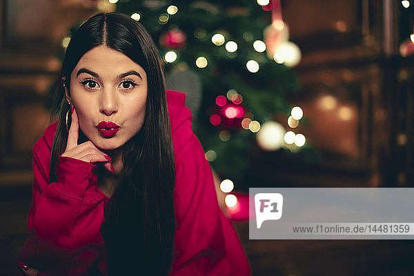 Porträt einer Teenagerin mit Weihnachtsbaum im Hintergrund und schmollendem Mund