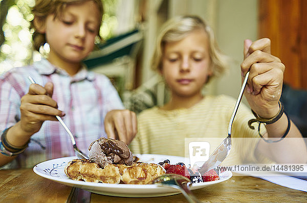 Zwei Jungen sitzen am Tisch und essen Eiscreme