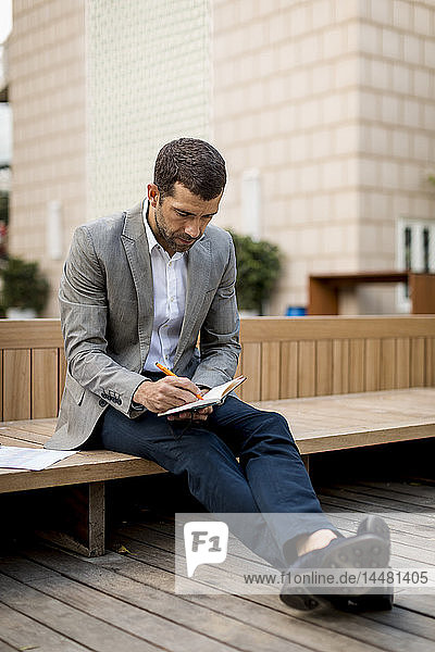 Businessman sitting on a bench writing into diary