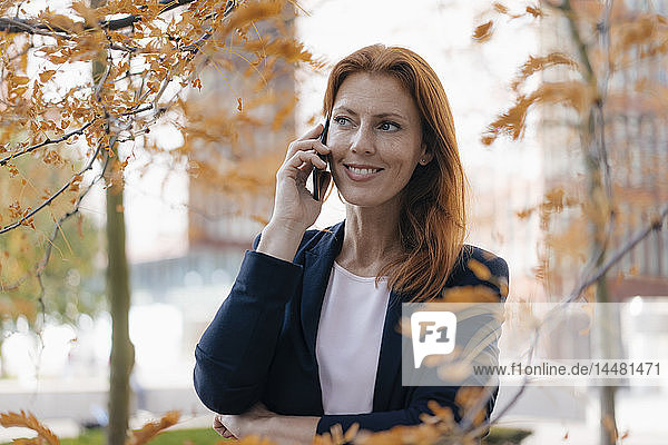 Lächelnde Geschäftsfrau am Handy im Herbst draußen in der Stadt