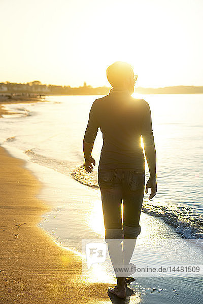 Silhouette eines Mannes  der bei Sonnenuntergang am Strand spazieren geht