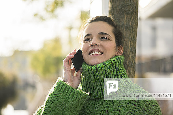Porträt einer glücklichen Frau am Telefon mit grünem Rollkragenpullover im Herbst