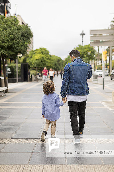 Rear view of father and son walking hand in hand in the city
