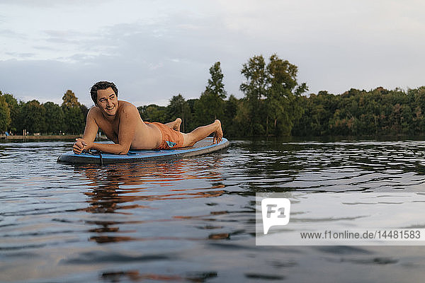 Mann liegt auf einem SUP-Brett auf einem See