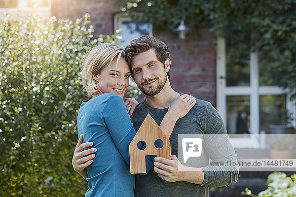 Porträt eines glücklichen Paares vor ihrem Haus mit Hausmodell