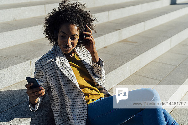 Schöne Frau sitzt auf einer Treppe in der Stadt  benutzt ein Smartphone  hört Musik mit Kopfhörern