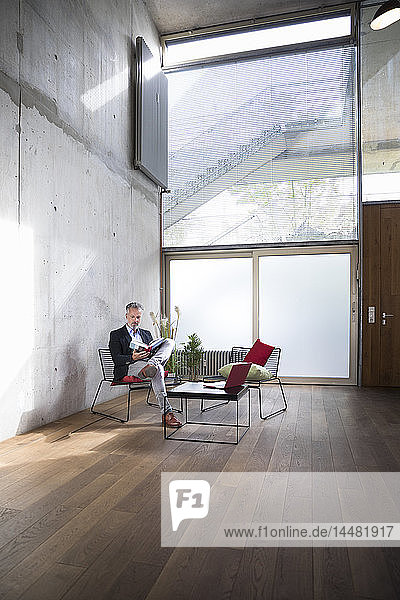 Businessman sitting in a loft at concrete wall reading book