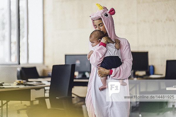 Junge Mutter trägt Einhorn-Einteiler  steht im Amt  hält ihren Sohn im Arm