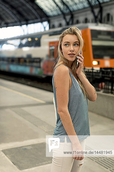 Junge Frau am Bahnhof am Handy  die sich umsieht