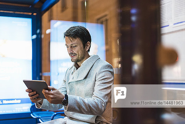 Geschäftsmann mit digitalem Tablett  der nachts an einer Bushaltestelle sitzt