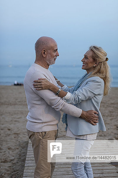 Spain  Barcelona  happy senior couple embracing on the beach at dusk