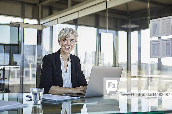 Porträt einer selbstbewussten Geschäftsfrau  die mit Laptop am Schreibtisch im Büro sitzt