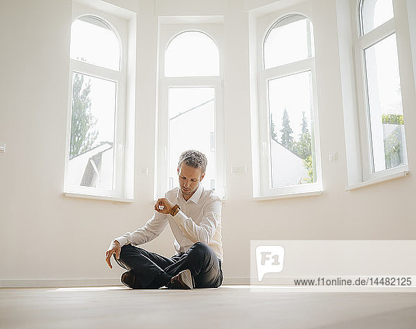 Geschäftsmann sitzt auf dem Boden seines frisch renovierten Hauses und prüft die Zeit