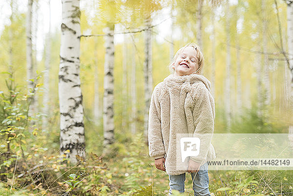 Porträt eines lachenden blonden Mädchens beim Spielen im herbstlichen Wald