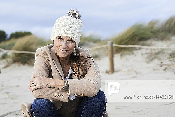 Spanien  Menorca  Porträt einer lächelnden älteren Frau mit Pudelmütze am Strand im Winter