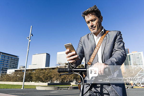 Mature businessman commuting in the city with his kick scooter  usine smartphone