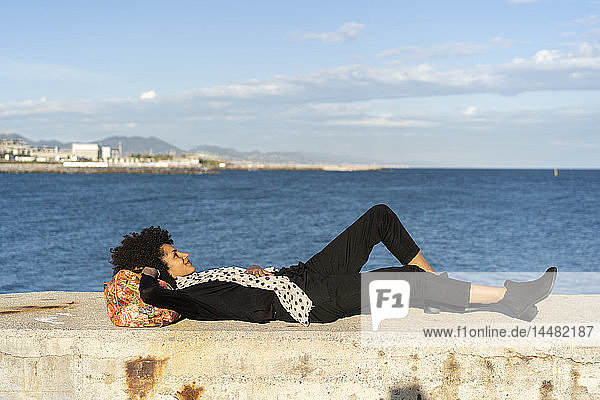 Spanien  Barcelona  schwarz gekleidete Frau entspannt sich auf einer Mauer vor dem Meer