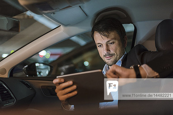 Geschäftsmann  der nachts im Auto sitzt und ein digitales Tablet benutzt