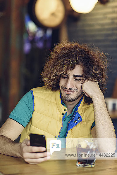 Portrait of smiling young man with beard and curly hair looking at cell phone in a pub