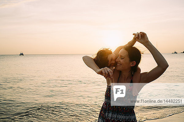 Thailand  Koh Lanta  glückliche Mutter mit Mädchen auf den Schultern am Meeresufer bei Sonnenuntergang