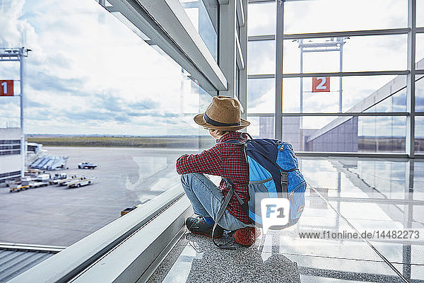 Junge sitzt auf dem Flughafen hinter einer Fensterscheibe und schaut auf den Flugplatz