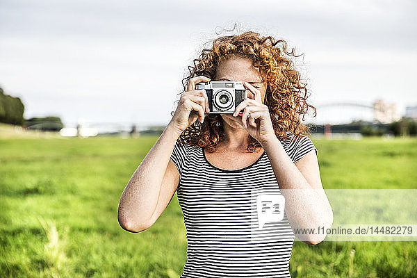 Young woman on a meadow taking picture of viewer with camera