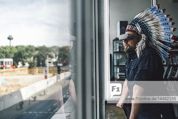 Mann mit indischem Kopfschmuck und VR-Brille im Büro  schaut aus dem Fenster