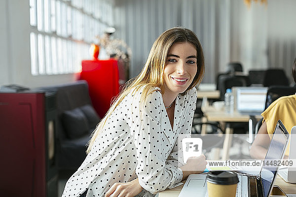 Porträt einer lächelnden jungen Frau am Schreibtisch im Büro