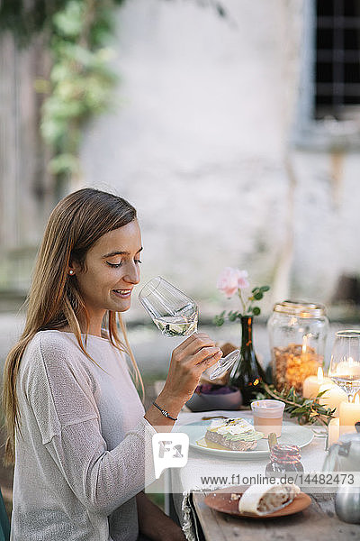 Frau probiert ein Glas Wein am Gartentisch