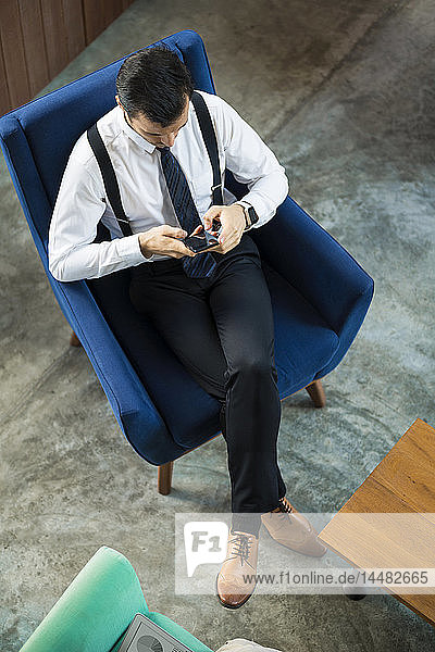 Top view of businessman sitting in blue armchair using smartphone