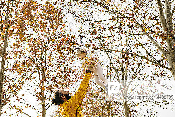 Vater wirft seine Tochter in die Luft  im Herbst in einem Park