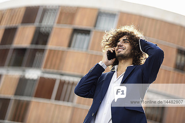 Portrait of young smiling fashionable businessman with curly hair on the phone