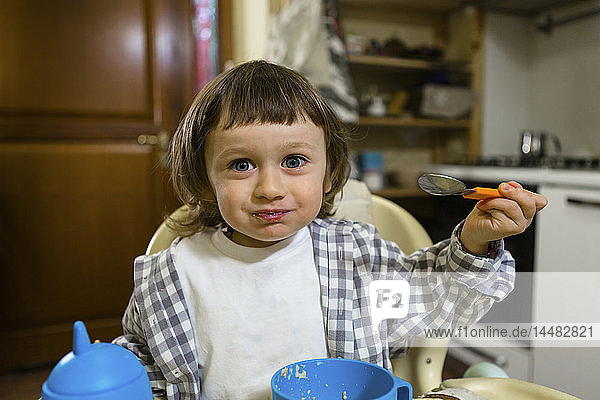 Porträt eines süßen Kleinkindes  das auf einem Hochstuhl in der Küche sitzt