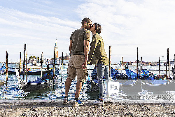 Italy  Venice  affectionate young couple kissing with gondola boats in background