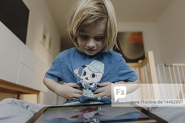 Portrait eines zufriedenen kleinen Jungen  der zu Hause ein digitales Tablet benutzt