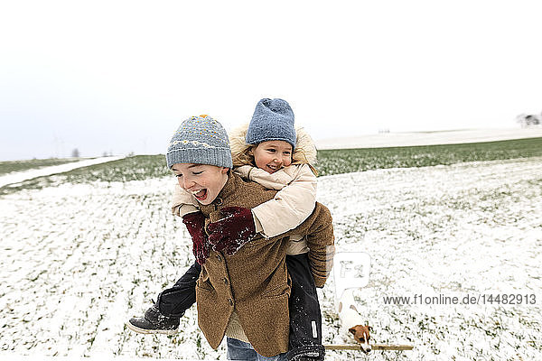 Boy carrying happy sister piggyback in winter landscape
