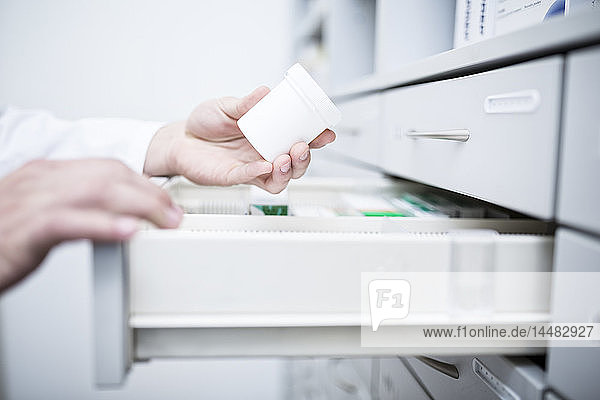 Close-up of pharmacist taking medicine from cabinet in pharmacy