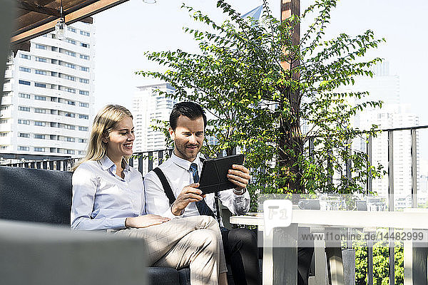 Smiling business colleagues on city terrace looking at tablet