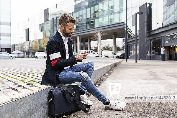 Stylish businessman sitting in the city using cell phone