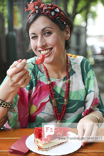 Frau isst Erdbeerkuchen in Straßencafé
