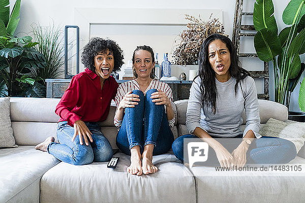 Drei aufgeregte Frauen sitzen zu Hause auf der Couch und sehen fern