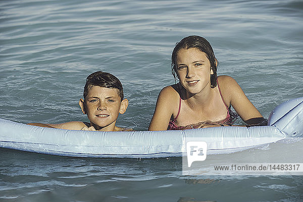 Lächelnder Bruder und Schwester schwimmen mit Schlauchboot