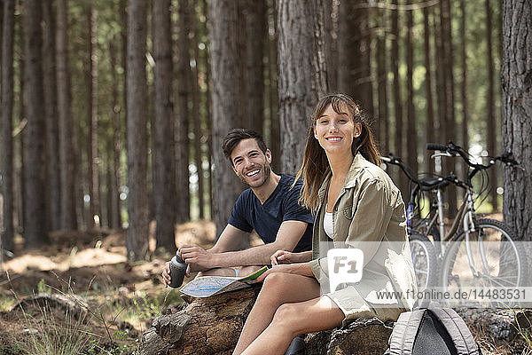 Lächelndes junges Paar sitzt auf einem Baumstamm im Kiefernwald