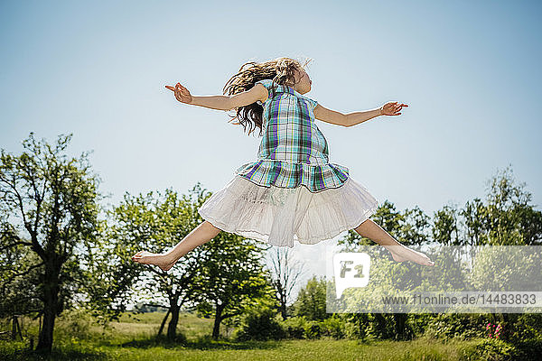 Unbekümmertes Mädchen im Kleid springt vor Freude im sonnigen Hinterhof