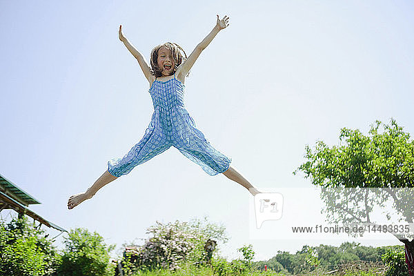 Porträt verspieltes  sorgloses Mädchen  das vor Freude im Hinterhof springt