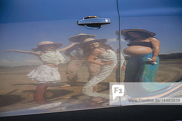 Spiegelung einer schwangeren Frau und ihrer Familie auf einer sonnigen Autotür