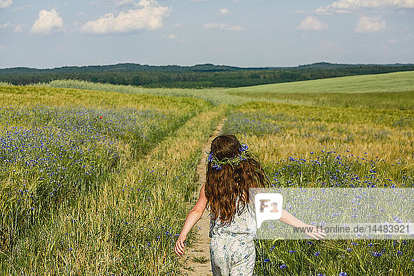 Mädchen  das in einem sonnigen  idyllischen  grünen Feld mit Wildblumen läuft
