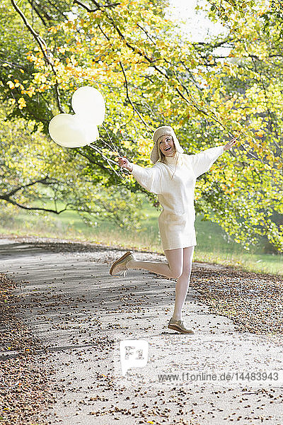 Sorglose Frau mit Luftballons im herbstlichen Park