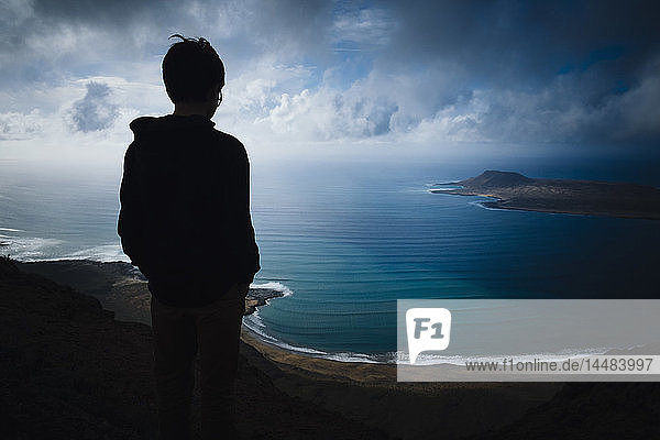 Junge mit Blick auf eine malerische Bucht mit Gewitterwolken über dem Meer  Lanzarote  Kanarische Inseln  Spanien